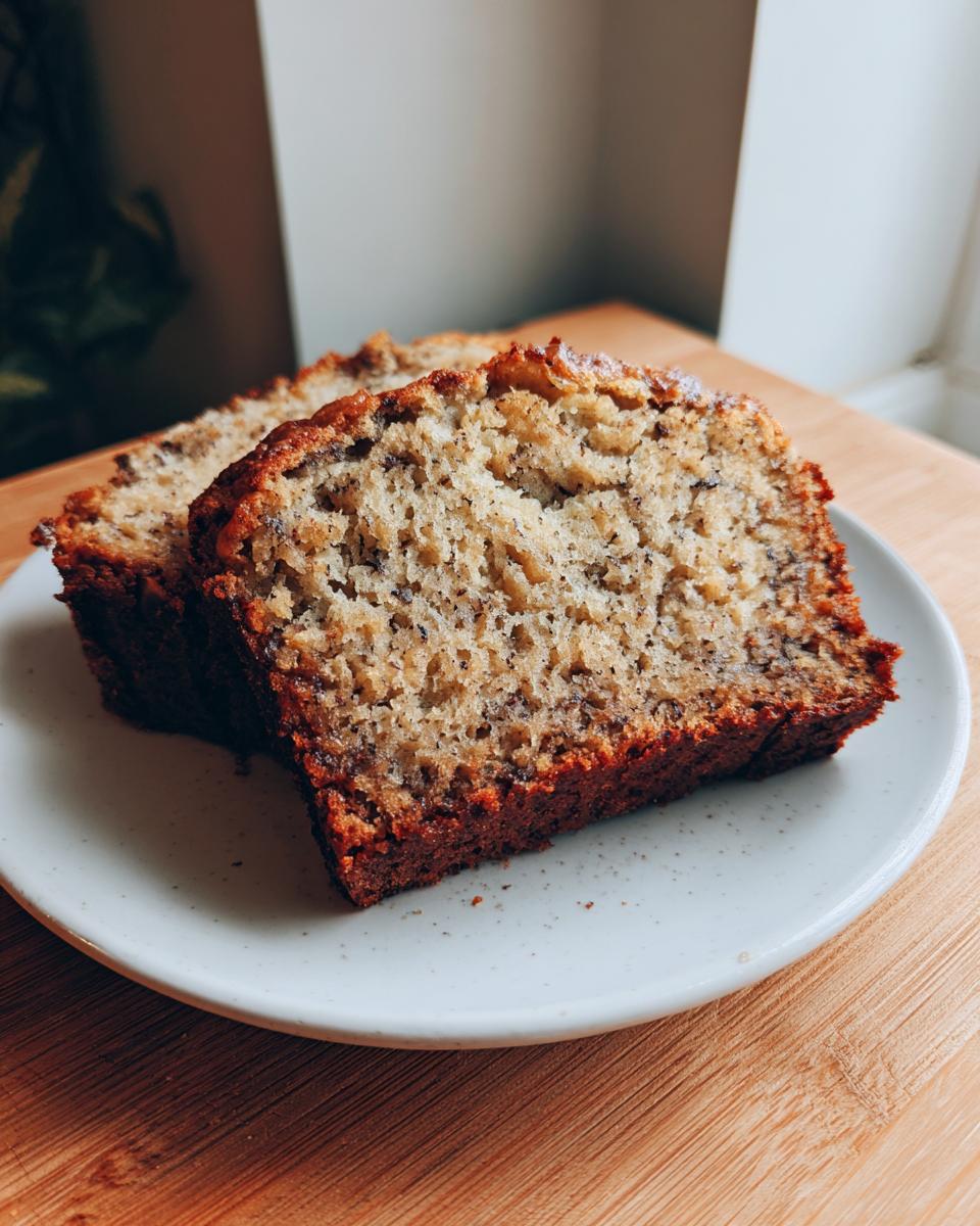 Two thick slices of moist banana bread recipe displayed on a speckled white plate.