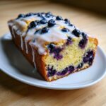 A slice of moist blueberry zucchini bread topped with a thick white glaze and fresh blueberries.