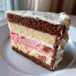 Close-up of a multi-layered slice of neapolitan cake showing chocolate, vanilla, and pink layers with white frosting.