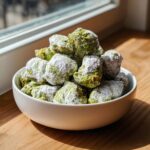 A white bowl overflowing with bright green pistachio puppy chow generously dusted with white powdered sugar.
