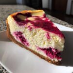 A perfect slice of creamy raspberry cheesecake featuring rich magenta swirls on a graham cracker crust.