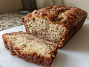 Close-up of freshly baked snickerdoodle banana bread loaf with one slice cut, showing a moist crumb and sugary topping.