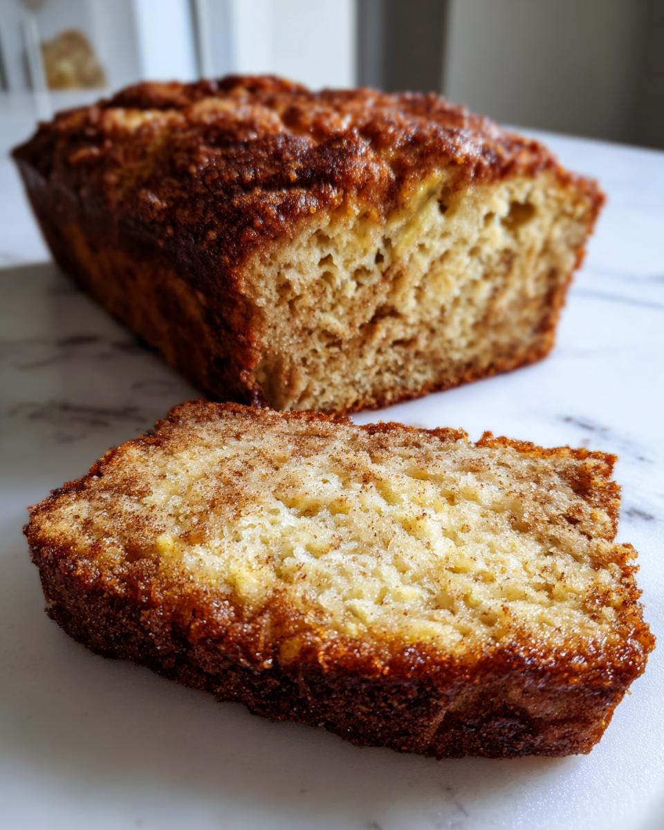 A close-up of a thick slice of snickerdoodle banana bread showing a moist crumb and cinnamon sugar crust.