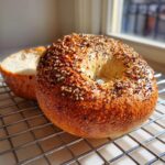 A freshly baked sourdough discard bagel topped with sesame and poppy seeds resting on a cooling rack.