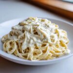 A serving of spaghetti generously topped with creamy cottage cheese alfredo sauce and black pepper.