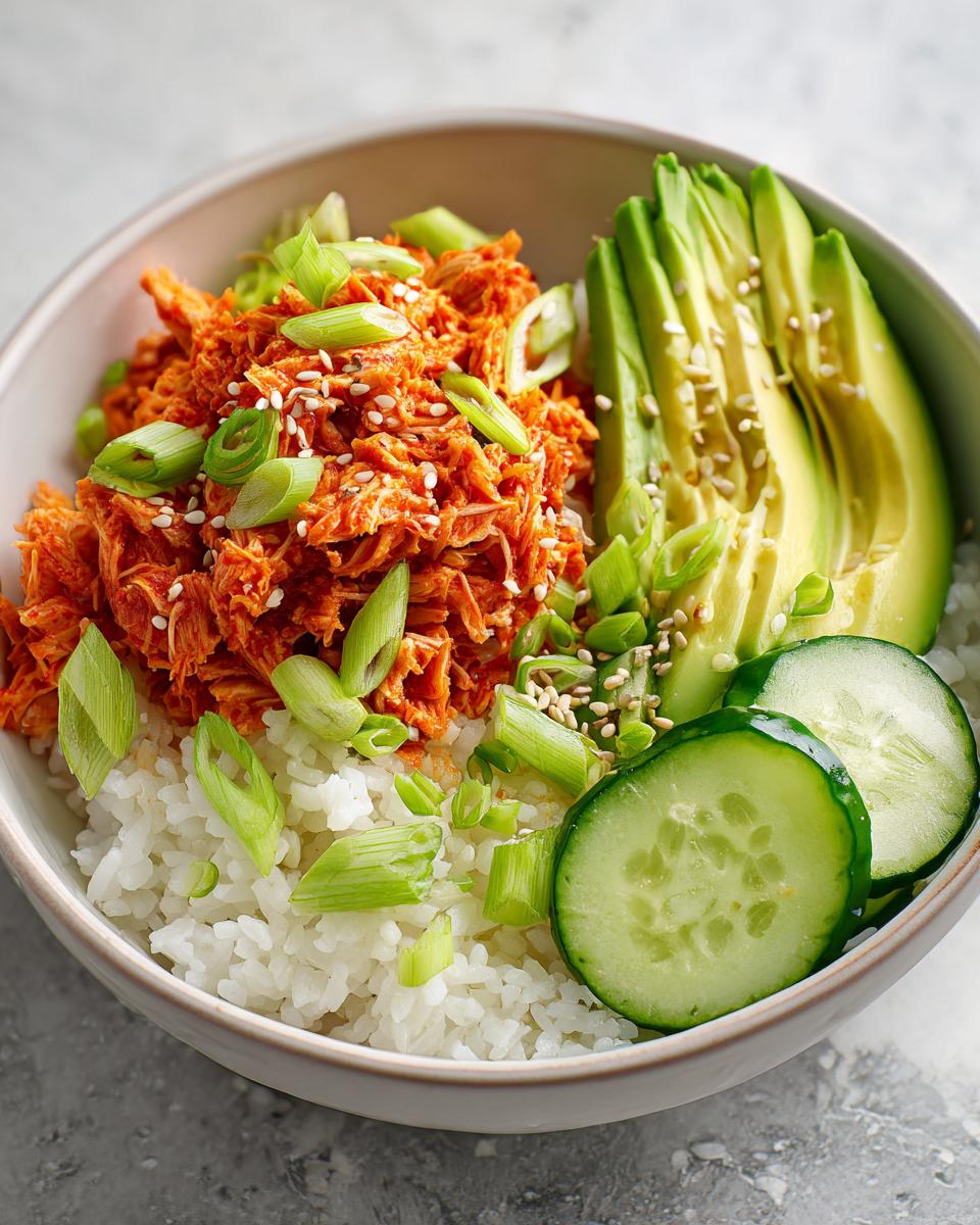 A close-up of a spicy crab sushi bowl featuring shredded spicy crab mix over rice, topped with sliced avocado, cucumber, and green onions.