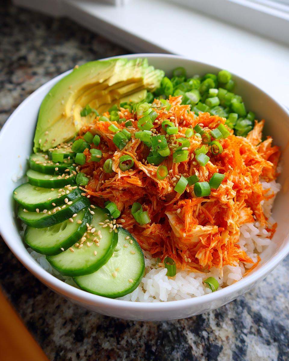 A vibrant spicy crab sushi bowl featuring shredded orange crab mix over rice, topped with sliced avocado, cucumbers, and green onions.