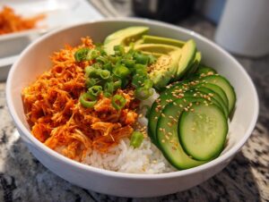 A white bowl filled with rice, topped with shredded spicy crab, sliced avocado, cucumber, and green onions.