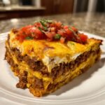 A delicious slice of layered taco pie topped with melted cheese, sour cream, and fresh pico de gallo.