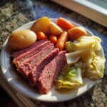 A plate featuring slices of tender corned beef next to boiled potatoes, carrots, and cabbage.