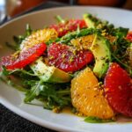 Close-up of a vibrant citrus salad featuring blood orange, regular orange slices, avocado, arugula, and chopped pistachios.