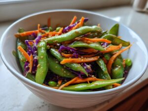 Close-up of a vibrant edamame salad featuring bright green edamame pods, shredded carrots, and purple cabbage, topped with sesame seeds.