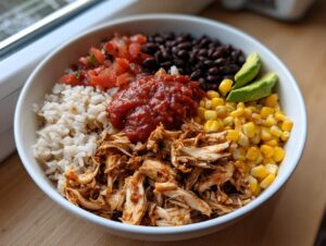 A vibrant, fully loaded chicken burrito bowl featuring shredded chicken, rice, corn, black beans, salsa, and avocado slices.