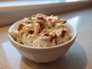 A close-up of the rich and creamy 5-minute million dollar dip topped with bacon bits and green onions in a white serving bowl.