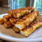 A close-up of crispy, golden brown air fryer halloumi fries stacked on a white plate, showing the soft white cheese inside.