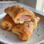 Close-up of three golden air fryer ham and cheese roll ups, one cut open showing melted cheese and ham.