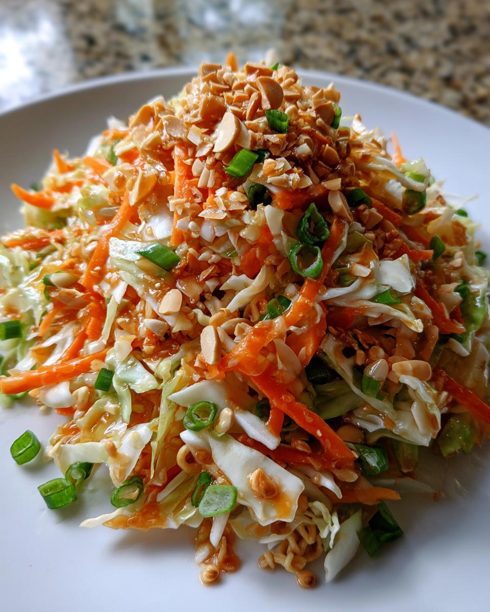 A vibrant mound of asian cabbage salad featuring shredded cabbage, carrots, and topped generously with crushed peanuts and green onions.