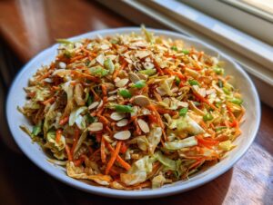 A vibrant bowl of asian ramen noodle salad featuring shredded cabbage, carrots, and topped with sliced almonds and green onions.