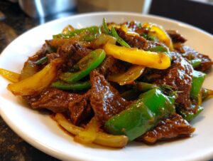 Close-up of delicious chinese pepper steak featuring tender beef strips, green bell peppers, and yellow onions in a savory sauce.