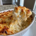 A spoonful of creamy, cheesy hot crab dip being lifted from a white baking dish, showing flaky crab meat.