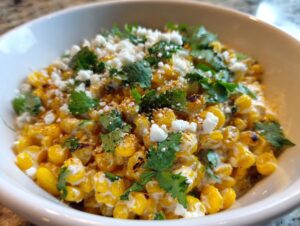 A close-up view of a creamy, vibrant street corn salad topped with crumbled white cheese and fresh cilantro.