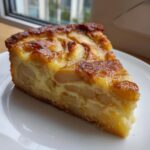 A close-up of a thick slice of apple custard impossible pie with a golden-brown, caramelized top.