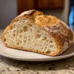 Close-up of a freshly baked artisan bread loaf, cut in half to show the airy, open crumb structure.