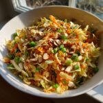 A vibrant bowl of asian ramen noodle salad featuring shredded cabbage, carrots, green onions, and toasted slivered almonds.
