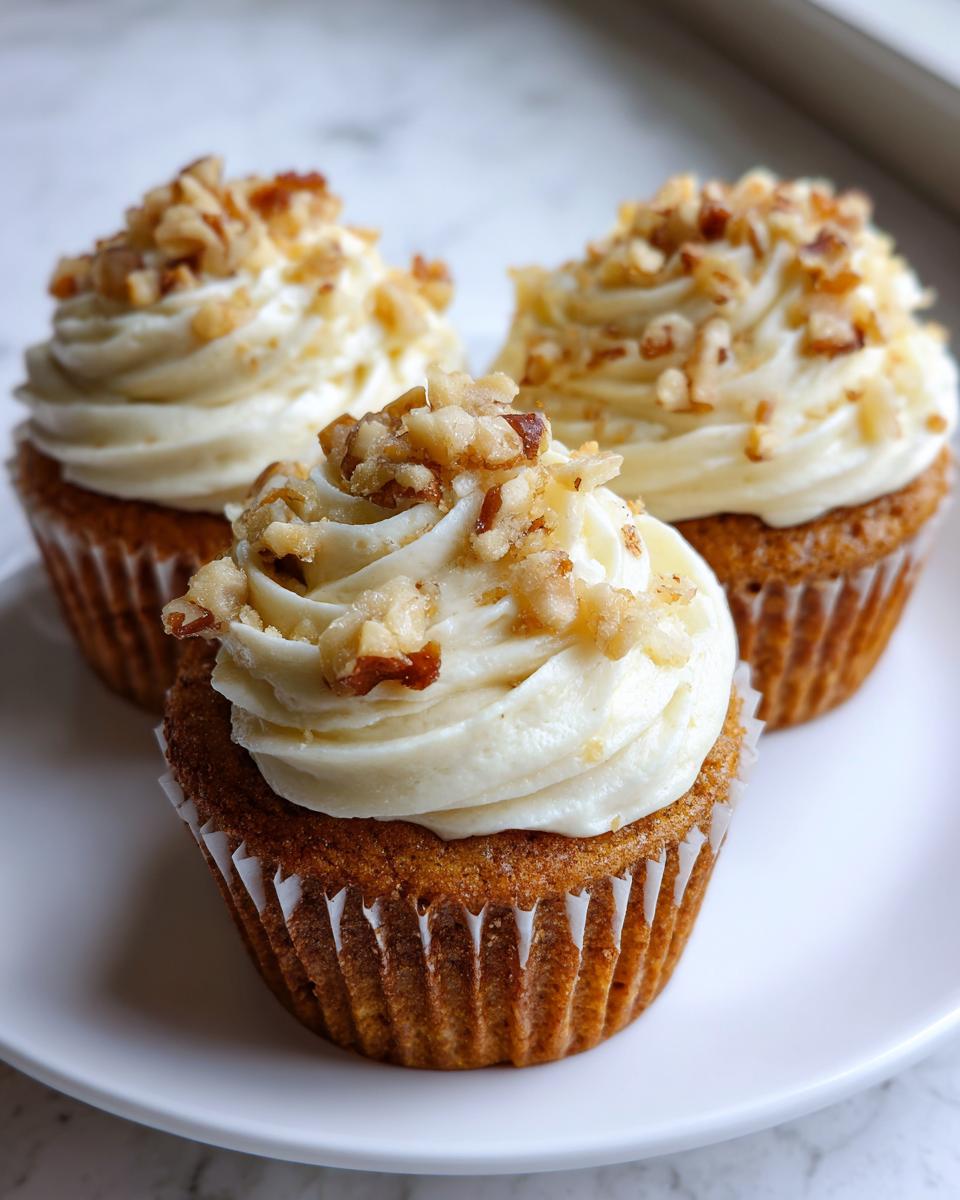 Three freshly baked banana walnut cupcakes topped with thick cream cheese frosting and chopped walnuts.