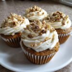 Four delicious banana walnut cupcakes topped with creamy white frosting and sprinkled with chopped walnuts.