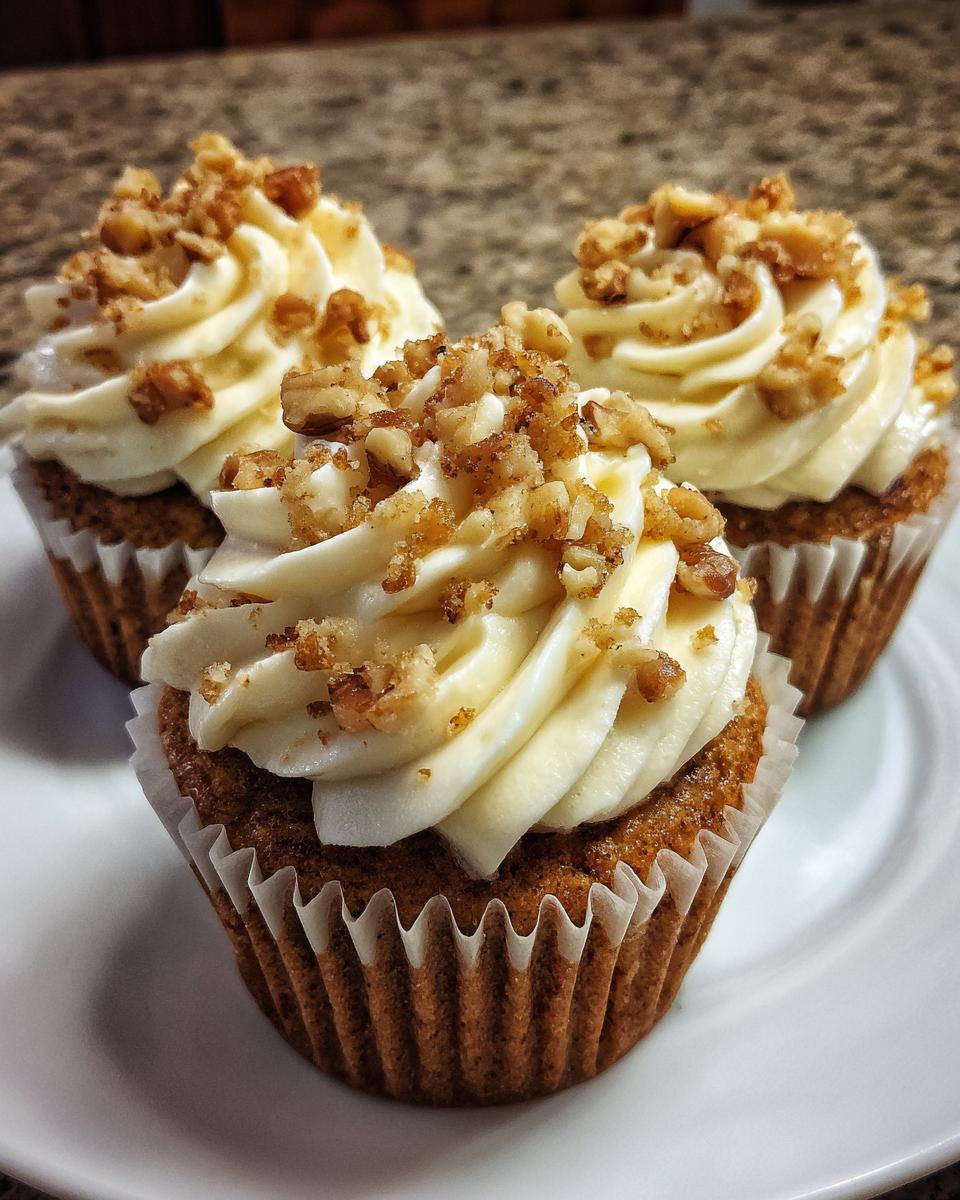 Three delicious banana walnut cupcakes topped with cream cheese frosting and chopped walnuts.