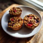 Three golden brown baked oatmeal cups with visible berries served on a light ceramic plate.
