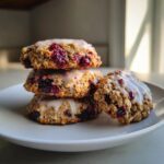 A stack of four berry iced oatmeal cookies topped with a sweet white glaze, showcasing visible oats and dark berries.