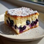 A close-up of one square of blueberry cream cheese cake, topped with powdered sugar.
