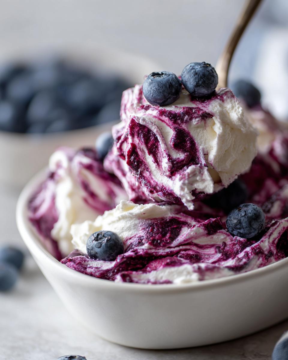 Close-up of a spoonful of creamy blueberry fluff salad swirled with purple blueberry puree and topped with fresh blueberries.