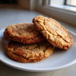 Three freshly baked brown butter sugar cookies stacked slightly on a white plate, coated in sparkling sugar crystals.