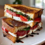 A grilled caprese breakfast sandwich, cut in half and stacked, showing mozzarella, tomato, basil, and balsamic glaze.