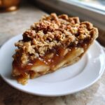 A close-up slice of caramel apple crisp pie showing a thick layer of gooey caramel apples and a crunchy oat topping.