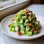 A mound of diced celery salad mixed with a creamy dressing and topped generously with walnuts.