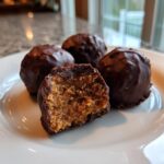 Close-up of chocolate chip cookie dough truffles, one cut in half showing the doughy interior coated in dark chocolate.