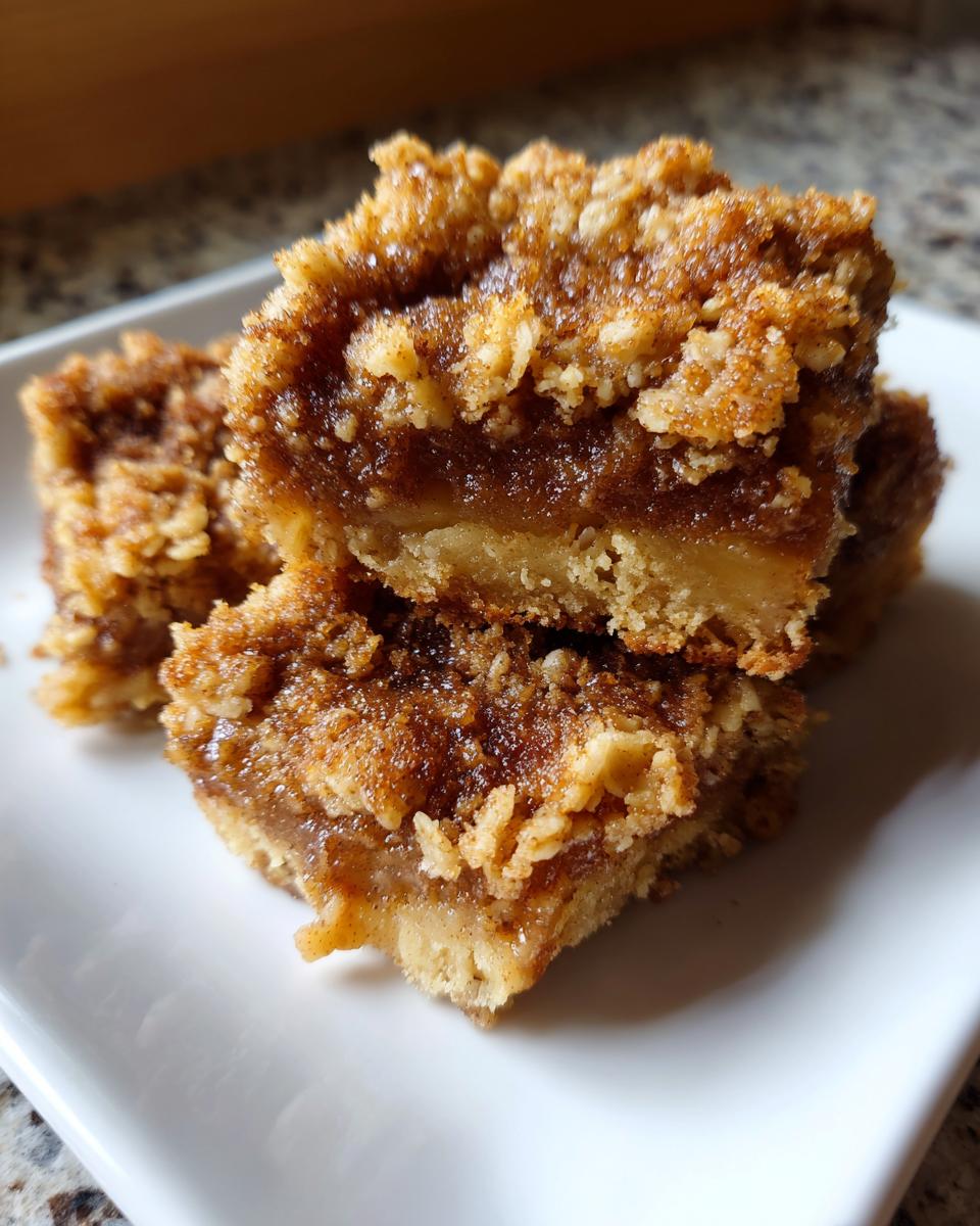 Close-up of three stacked, gooey cinnamon apple crisps bars with a thick, crumbly topping.