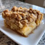 A close-up of a square serving of warm cinnamon apple crisps with a thick, crumbly oat topping.