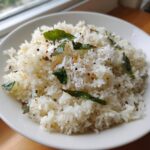A close-up of fluffy white coconut pepper rice garnished with shredded coconut, curry leaves, and spices.