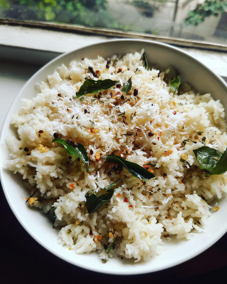 A white bowl filled with fluffy coconut pepper rice, topped with grated coconut, pepper flakes, and curry leaves.