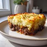 A thick slice of homemade cottage pie showing a rich meat base and a golden, fluffy mashed potato topping.