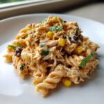 A close-up serving of creamy chipotle chicken pasta salad featuring rotini pasta, shredded chicken, corn, and black beans.