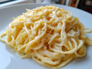 A close-up shot of creamy spaghetti coated generously in a rich parmesan pasta sauce on a white plate.