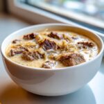 Close-up of a hearty bowl of philly cheese steak soup, featuring chunks of beef and caramelized onions in a creamy sauce.