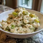 Close-up of creamy dill pickle chicken salad featuring shredded chicken, celery, and pickle chunks in a white bowl.