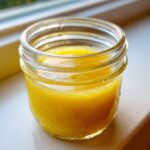 Close-up of bright yellow easy lemon vinaigrette dressing mixed in a small glass jar.